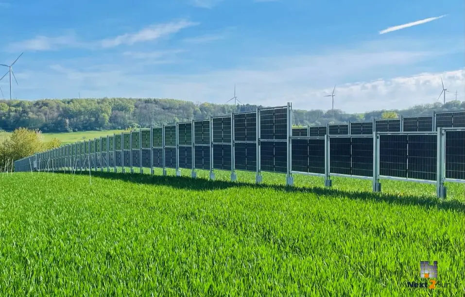 Solarzaun-Linie über flaches Weideland mit Windrädern